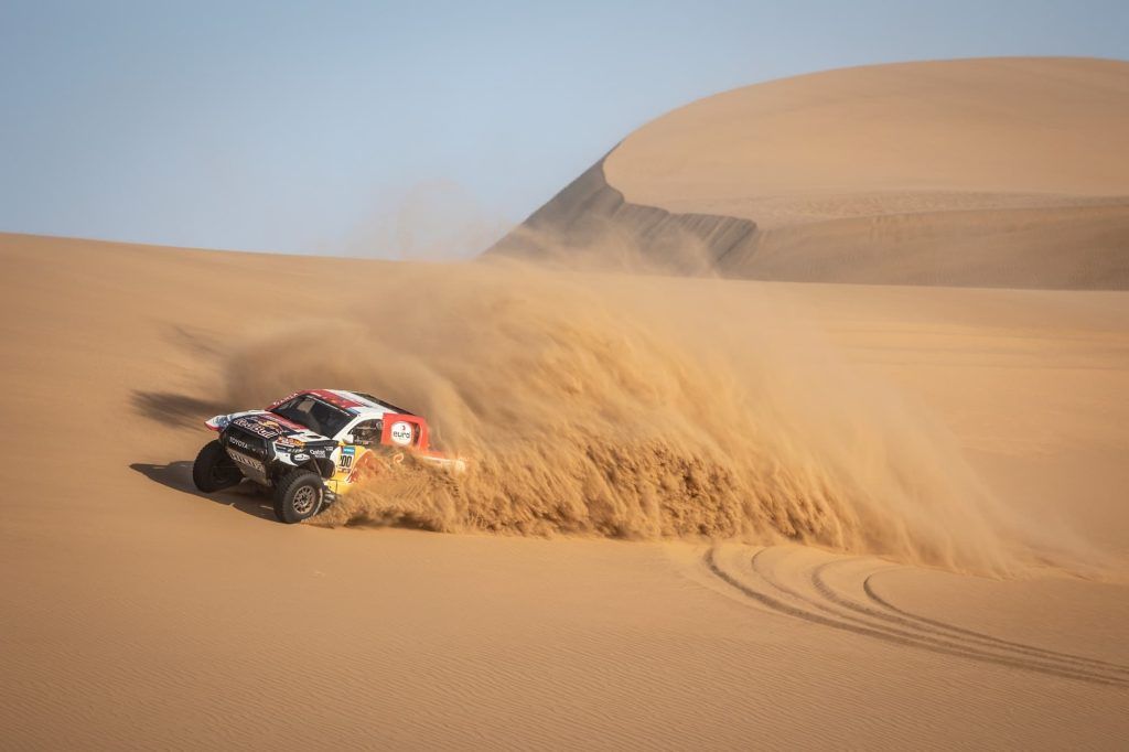 Coche de rally avanzando por una pista de arena durante una etapa del Dakar.